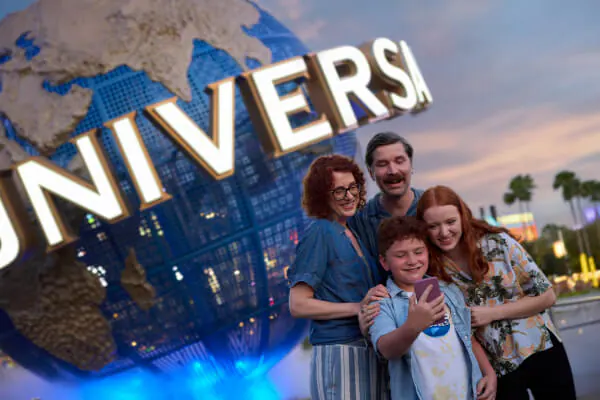 A family of four smiling excitedly as they pose for a selfie together in front of the iconic Universal globe.