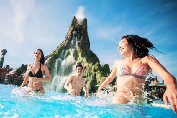 Guests&nbsp;enjoy&nbsp;Waturi&nbsp;Beach&nbsp;at&nbsp;Volcano&nbsp;Bay&nbsp;with&nbsp;Krakatau&nbsp;volcano towering&nbsp;in&nbsp;the&nbsp;background.