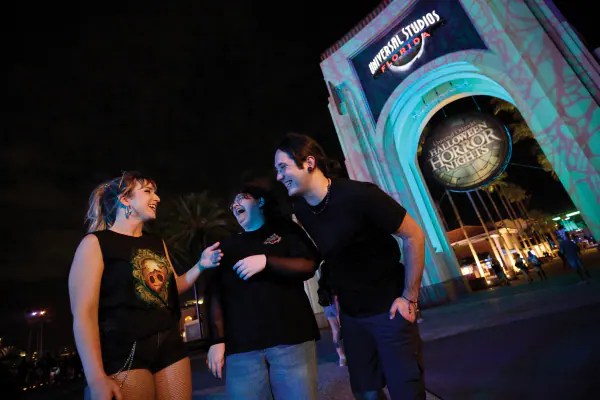 Friends laughing in front of the eerily lit Universal Studios Florida entry arch with a Halloween Horror Nights sign.