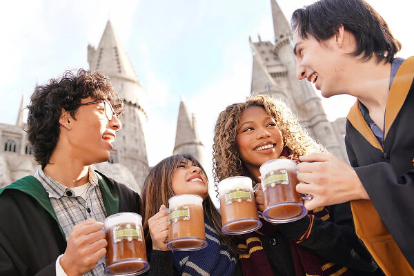 A group of friends dressed in Hogwarts™ student robes, laughing and enjoying frozen Butterbeer™ at Hogsmeade™.
