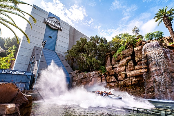 A boat from Jurassic World – The Ride at Universal Studios Hollywood creates a large spash at the bottom of a water flume.