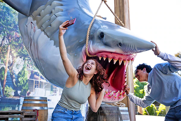 Two friends laugh and pose for a selfie next to Jaws from Universal Studios Hollywood.