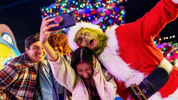 Three friends laughing as they pose for a selfie with the Grinch with colorful Christmas decor in the background
