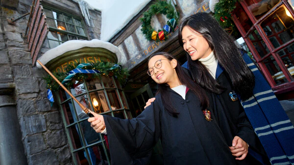 A daughter holding her wand in the air with her mother smiling behind her in front of storefronts decorated for the holidays.