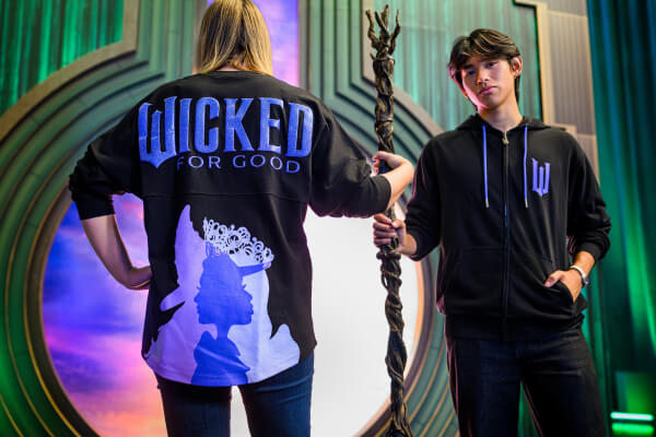 Two models wearing Wicked: For Good merchandise featuring Elphaba and Glinda s silhouettes.
