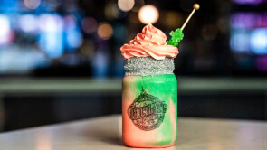 A pink and green milkshake with a WICKED branded garnish on top.