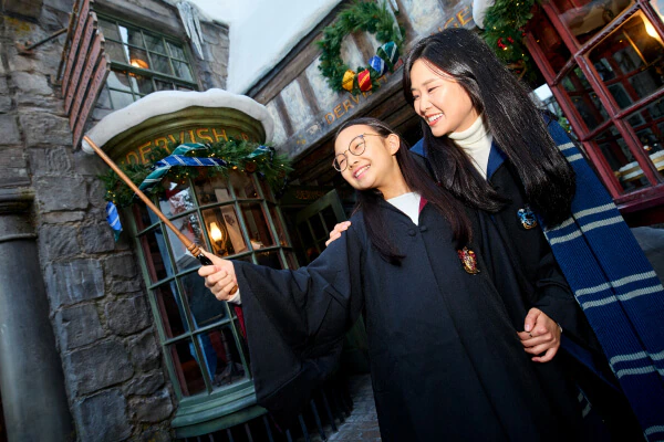 A daughter holding her wand in the air with her mother smiling behind her in front of storefronts decorated for the holidays.