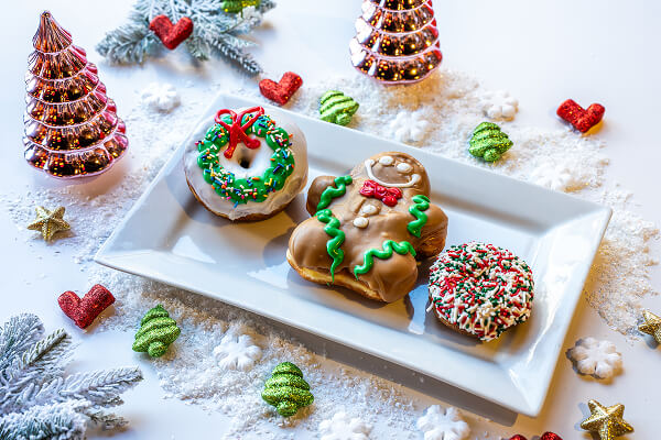 A plate with a frosted and sprinkled gingerbread figure and donuts on a snowy surface with holiday greenery and decorations.