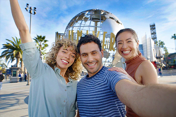 Three people posing for a selfie in front of the Universal Studios Hollywood sign.