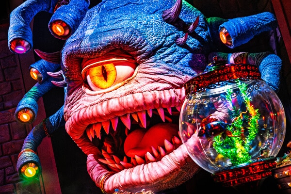 The blue, many-eyed creature Xanathar baring his teeth alongside a floating fishbowl and a collection of golden treasures.
