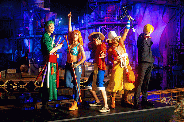 Rotating GIF of a “ONE PIECE PIRATE SHOW” animated scene and live characters in colorful costumes on a floating wooden stage.
