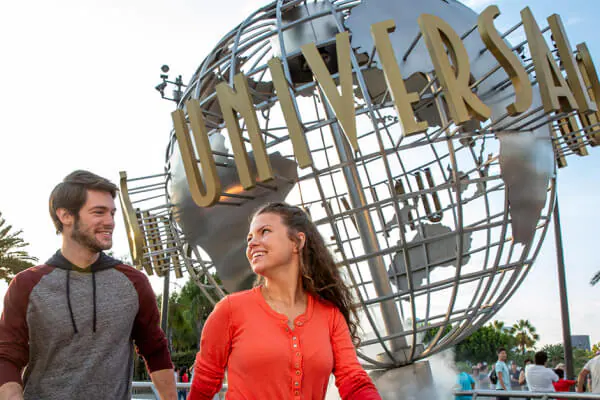 A couple holding hands and smiling at each other walking past the iconic Universal globe with other Guests in the background.