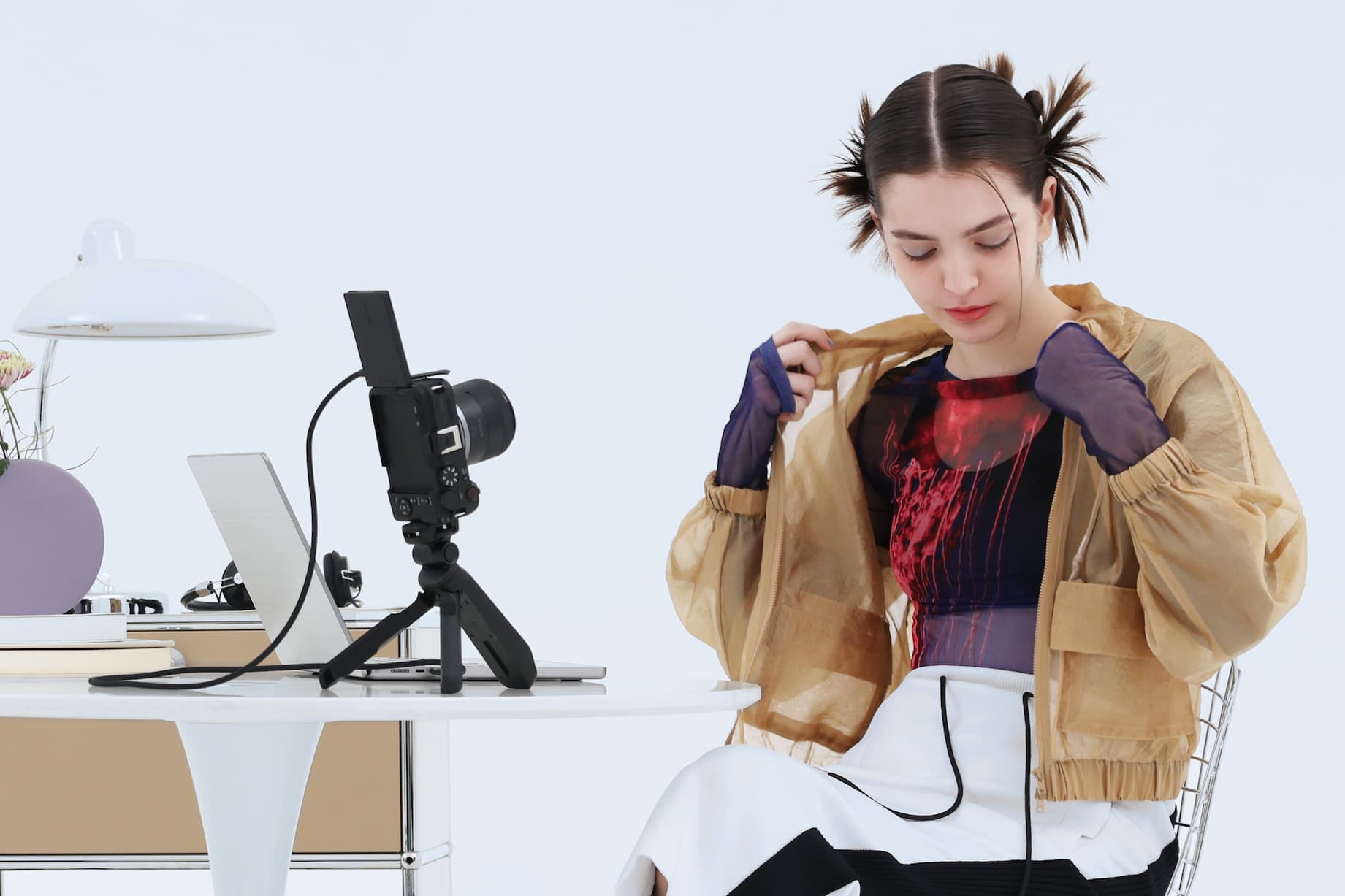 A woman sits at a desk. On the table in front of her, a camera on a small tripod