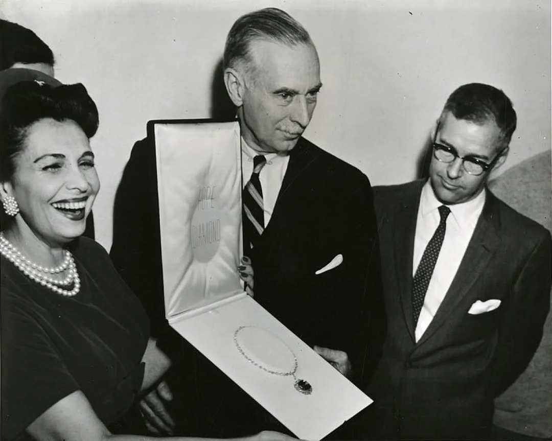 A black and white photo of a woman and two men holding a case displaying the Hope Diamond