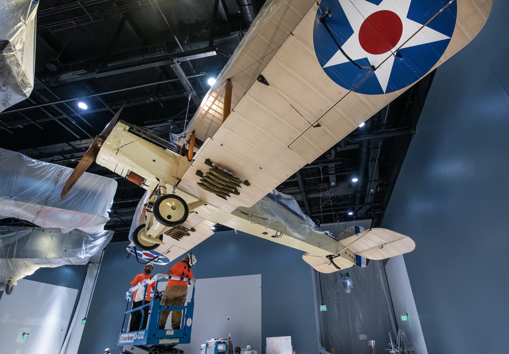 A vintage aircraft being lifted to be hung from the ceiling.