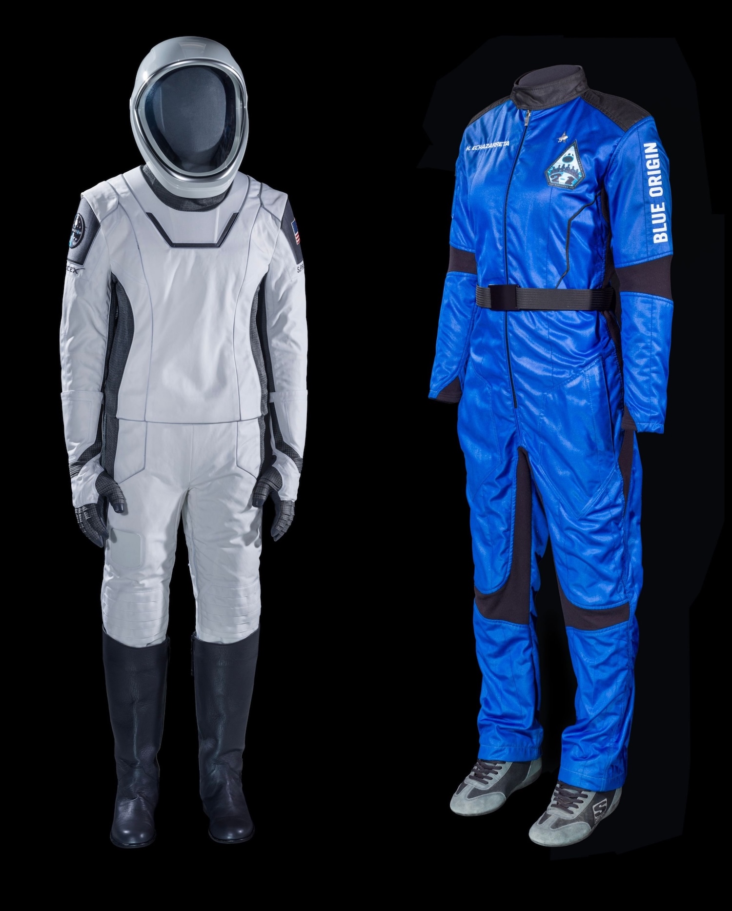 Two spacesuits side by side with a black background. The one of the left is white and gray with a helmet. The one on the fight is a royal blue.