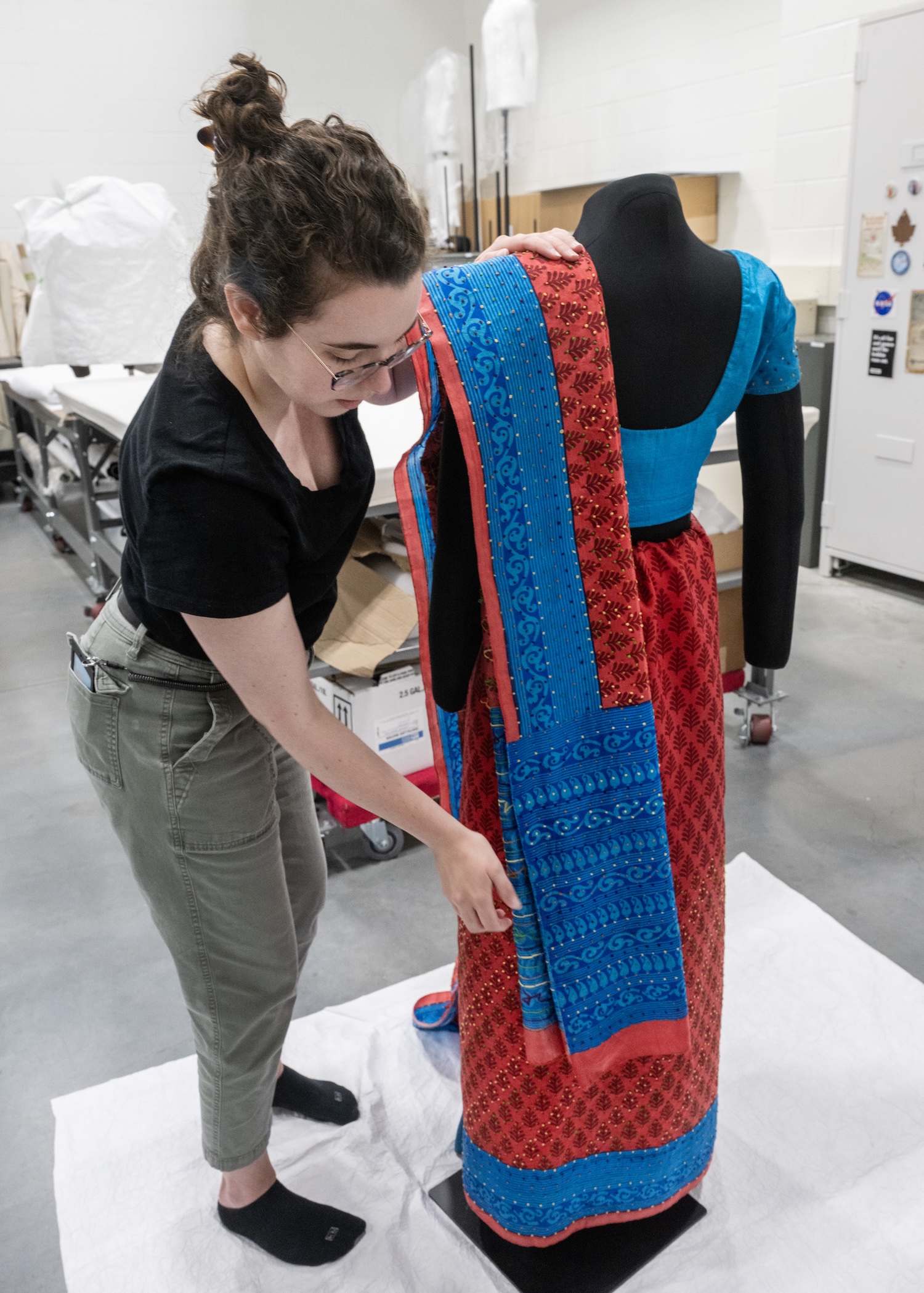 A woman positions a saree on a mannequin.
