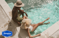 Two people sit at the edge of the pool at Hampton East Austin in Austin, Texas