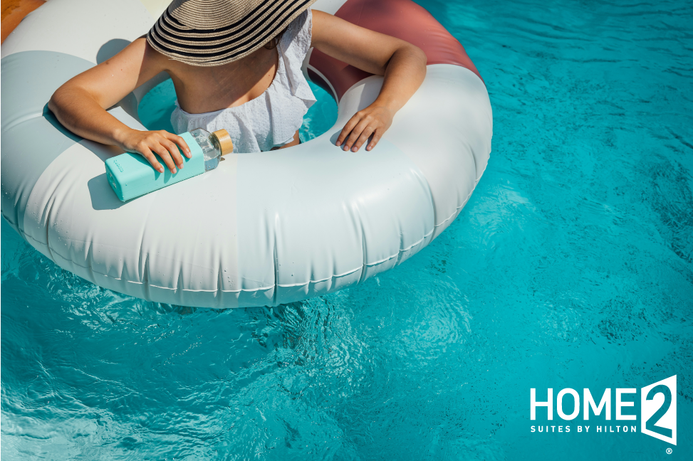 A woman wearing a straw hat floats in an inner tube in a pool at Home2 East Austin