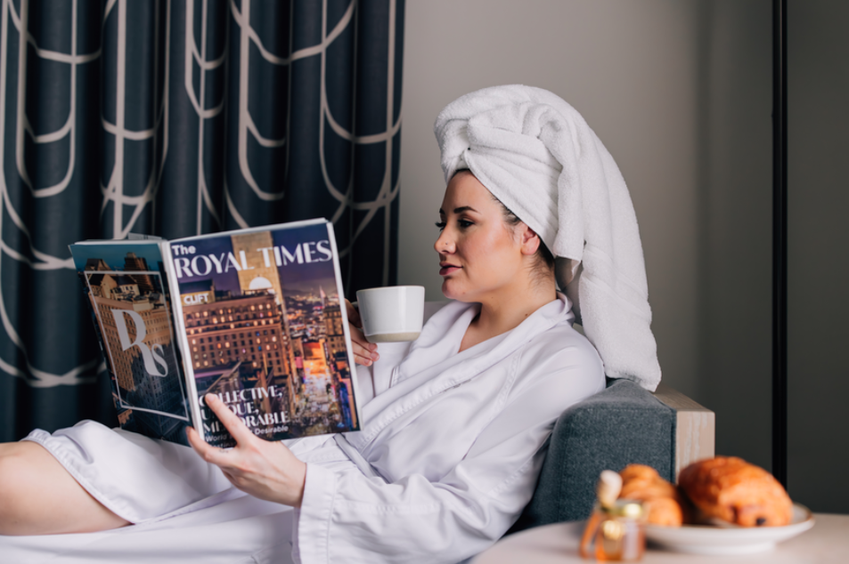 Woman wearing a robe reads a magazine and holds a coffee cup in a room at The Stephen F. Austin Royal Sonesta Hotel