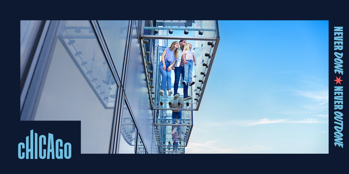 A view from below of two adults and a child inside the glass-enclosed Ledge at Skydeck Chicago