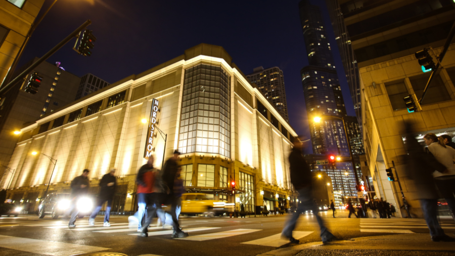 Shoppers pass by an illuminated building at night on The Magnificent Mile