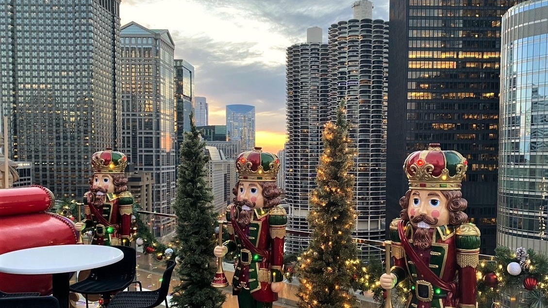 A hotel rooftop decorated with large nutcrackers and lit trees overlooks the city skyline