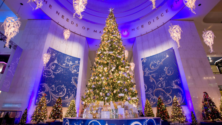 A huge decorated Christmas tree surrounded by smaller lit trees in the rotunda of the Griffin Museum of Science and Industry
