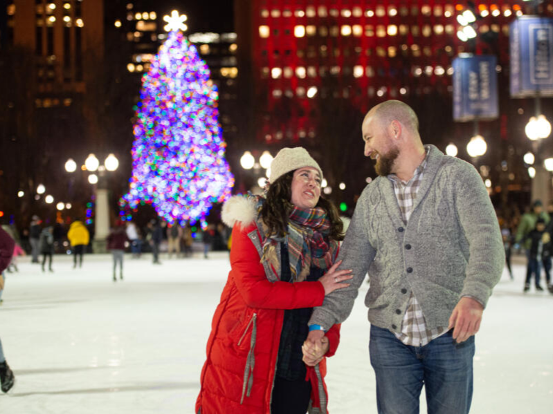 A couple skates on the McCormick Tribune Ice Rink in Millennium Park with the brightly lit City of Chicago Christmas tree in the background