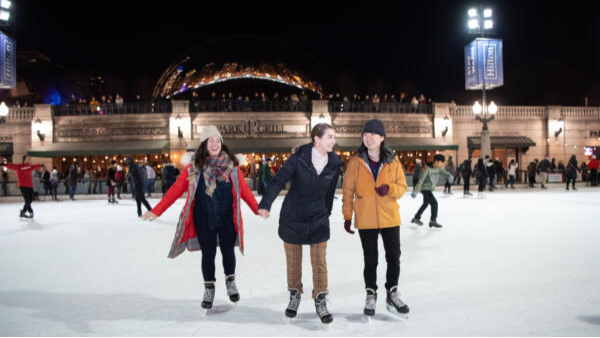 Three people ice skating together at Millennium Park ice skating rink.
