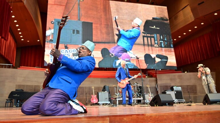 A performer at Chicago Blues Festival plying a guitar on stage on his knees