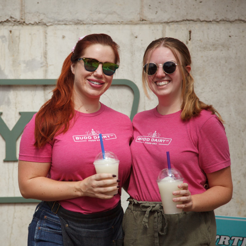 Image of two Budd Dairy employee holding beverages