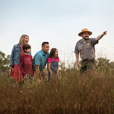 Site guide leads excited family through grassy field of a dig site