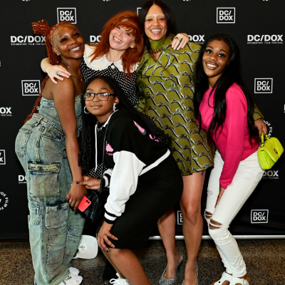 A group of five individuals pose closely together in front of a DC/DOX backdrop.
