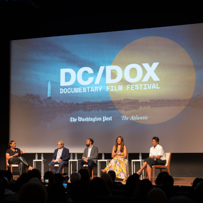  A panel discussion at the DC/DOX Documentary Film Festival with five participants, including filmmaker Dawn Porter, seated on chairs in front of a screen.