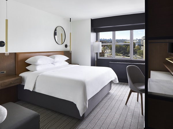 A sleek, modern king guest room with a large window view, featuring minimalist furniture and bright natural lighting.