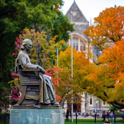 A bronze statue seated among colorful autumn foliage on the campus of George Washington University in Washington, DC.