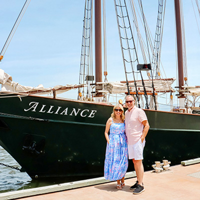 A couple poses in front of a tall ship before their daytime sail with Yorktown Sailing Charters.