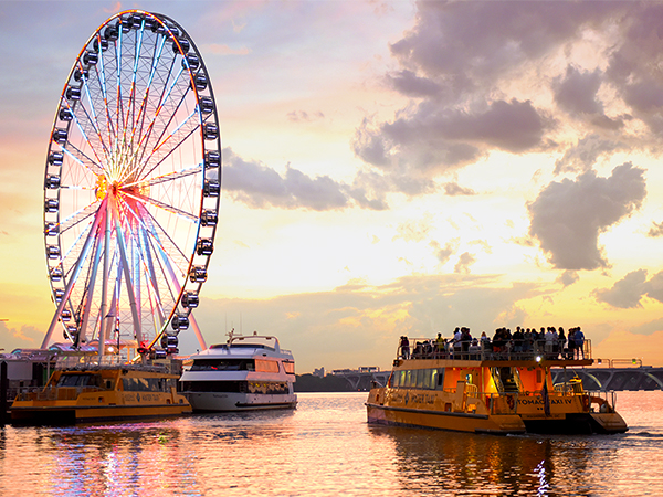 Boats float on the water at National Harbor beside the Capital Wheel. 