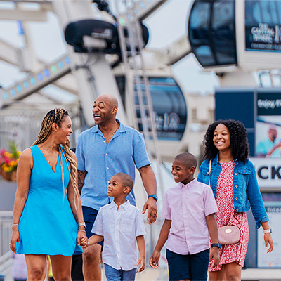  A mom, dad and three children laughing and walking along the National Harbor waterfront. 