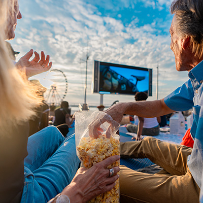 A man and woman smiling in front of a giant movie screen against the Potomac River. 