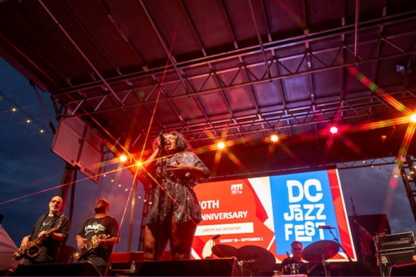 A band performs on an outdoor stage under colorful lights during DC JazzFest in Washington, DC.