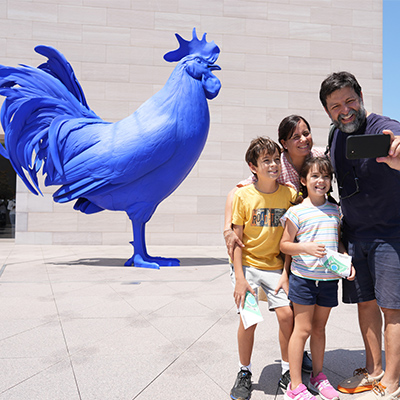 A family takes a selfie in front of the giant blue rooster sculpture at the National Gallery of Art in Washington, DC.