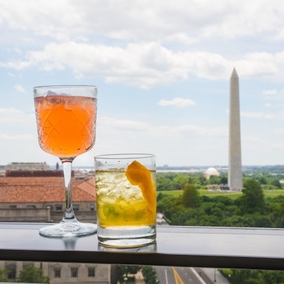 Two cocktails sit on a rooftop ledge with a clear view of the Washington Monument.