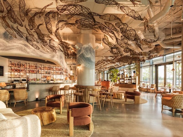 A spacious lounge at Fish Shop Bar & Restaurant showcases artistic ceiling sculptures above a modern bar and seating area.