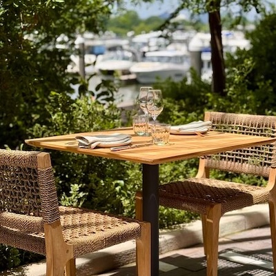 A neatly set outdoor dining table overlooks a marina with boats.