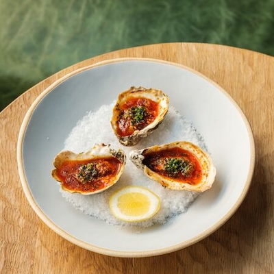 A plate of Tall Timbers oysters grilled with ‘nduja butter sits on a table. 