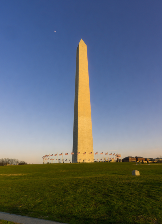 The Washington Monument stands tall under a clear evening sky with the moon visible above in Washington, DC.
