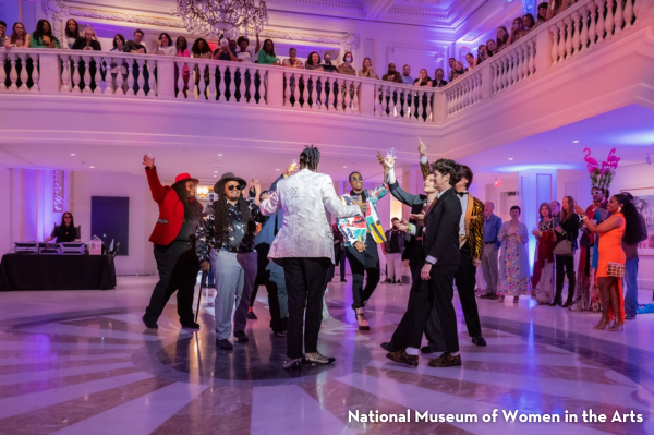 A group of people dancing and raising glasses in the grand hall of the National Museum of Women in the Arts.