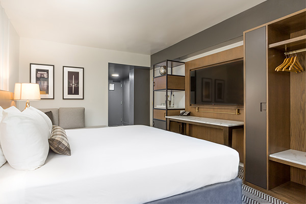 A modern guest room at Arc Hotel in Washington, DC featuring a large bed, wall-mounted TV, and open closet.
